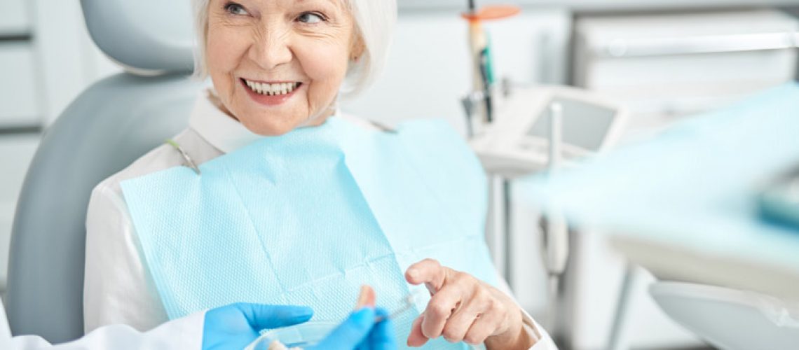 An image of an older woman sitting in a dental chair after a dental implant procedure